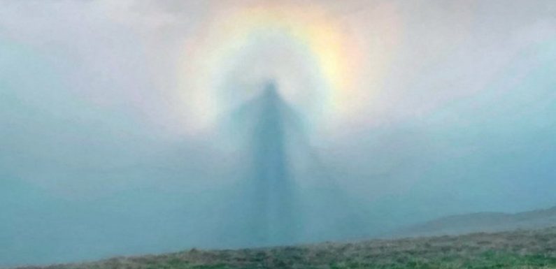 Un randonneur photographie une silhouette angélique dans le ciel entouré d’une auréole arc-en-ciel